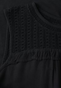 Top nero con un yoke in maglia testurizzata con bordo arricciato e una parte inferiore in tessuto liscio. Il design è completamente nero.