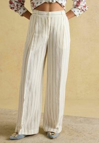 Pantaloni bej cu croială largă, cu dungi verticale și închidere cu nasturi. Confecționați dintr-un material ușor, cu pliuri în față și croială lejeră.