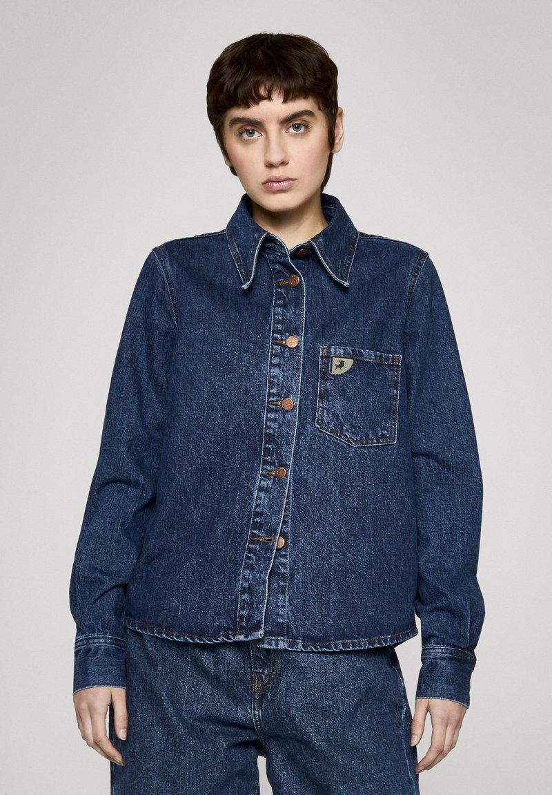 Ciemnoniebieska kurtka dżinsowa z rozłożystym kołnierzem, guzikami z przodu, kieszenią na piersi z naszywką z logo oraz długimi rękawami zakończonymi mankietami zapinanymi na guziki.