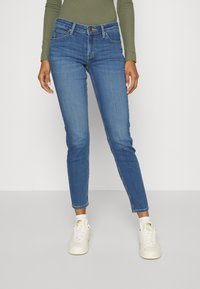Blå denim skinny jeans med en medelhög midja, två framfickor och en subtil slitningseffekt. Kombinerat med vita sneakers.