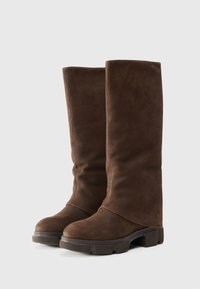 Brown suede knee-high boots with a slouchy design, rounded toe, and chunky rubber sole. Different textures visible on the upper.
