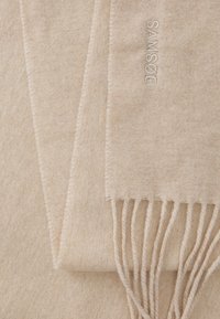 Beige sjaal van zacht materiaal, met een subtiele textuur, franjes aan de uiteinden en geborduurd merk in een bijpassende kleur.