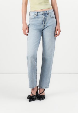 Jeans en denim bleu clair taille haute avec une coupe droite. Associés à des chaussures en vernis noir avec un accent de nœud.