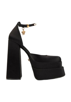 Chaussure à talon haut plateforme noire avec talon bloc épais, bride à la cheville et détail de pendentif doré près de la boucle.