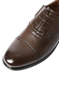 Scarpa da cerimonia in pelle marrone con allacciatura chiusa, punta a cappuccio, perforazioni decorative e finitura lucida su sfondo bianco.