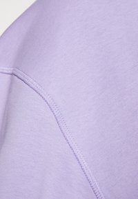 Dettaglio della cucitura di un tessuto lavanda che mostra cuciture fini e una trama a maglia liscia, evidenziando la qualità della costruzione del capo.