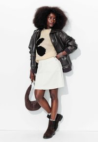 Veste en cuir noir épaisse, pull ivoire avec motif noir, jupe en velours côtelé blanche, bottes chelsea en suede marron et sac à main en tissu marron.