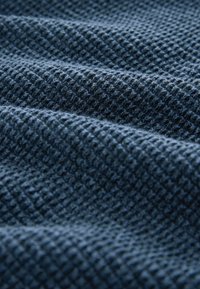 Texturiertes blaues Gewebe mit einem Karomuster, das ein gewebtes Design zeigt. Das Material scheint weich, dick und in einigen Bereichen leicht erhöht zu sein.