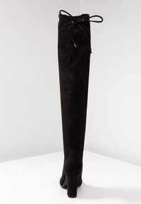 Botas negras sobre la rodilla hechas de suave gamuza, con una puntera redonda, tacón cuadrado y un lazo en la parte superior para un ajuste ajustable.