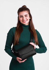 Černá kožená křížová taška se strukturálním tvarem, vybavená klapkovým uzávěrem, nastavitelného popruhem a embosovaným logem.