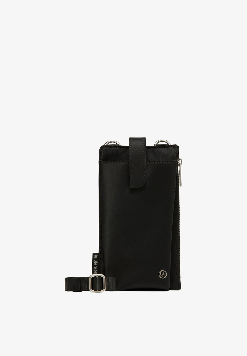 Borsetă verticală neagră cu clapetă frontală, fermoar lateral, curea reglabilă și un mic logo metalic circular în colțul din dreapta jos.