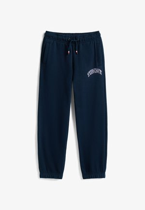 Pantalons de survêtement bleu marine en tissu doux, avec des poignets élastiqués, des poches latérales et un logo "TOMMY" brodé en blanc.