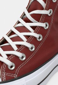 Punane kanvas tennisjalats valgete paeltega, hõbedaste silmadega ja kontrastse musta äärega taldal. Omab tekstureeritud ülemist osa ja puhtaid õmblusi.