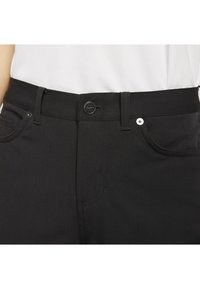 Black pants with belt loops, front button, and front pockets worn with a white tucked-in top.