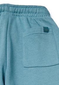 Helle blaue gestrickte Jogginghose mit elastischem Bund, einer Gesäßtasche und einem kleinen Markenetikett. Glatte Textur mit lockerer Passform.