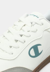 Hvit sneakers med teksturert overmateriale, lyseblå logo og klassisk snøring. Gummisåle med grå detaljer.