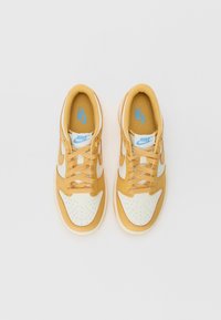 Nike sneakers med en gul overdel, hvite skinnoverleggs og blå logo detaljer. Har en perforert tåboks og runde snører.