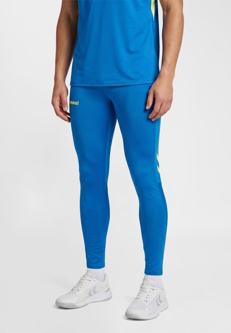 Man draagt felblauwe sportlegging, bijpassend top, witte sneakers en witte sokken tegen een lichte effen achtergrond.