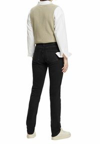 Chaleco de punto beige claro sobre una camisa blanca, combinado con jeans negros y zapatillas beige. El conjunto presenta un ajuste casual y minimalismo en los detalles.