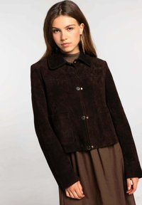 Chaqueta de ante marrón oscuro con cuello, cierre frontal de botones y dos bolsillos laterales. Presenta un tejido texturizado y líneas limpias.