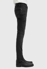Schwarze Slim-Fit-Jeans aus strukturiertem Denim-Stoff mit Vorder- und Hintertaschen, kombiniert mit schwarzen Leder-Stiefeletten.