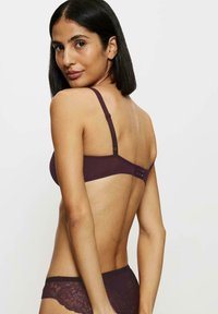 Burgundowy bralet z regulowanymi ramiączkami i zapięciem z tyłu; wyróżnia się gładkim materiałem, zapewnia minimalne zakrycie i nowoczesny design.