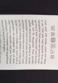 Waslabel met meertalige wasinstructies en symbolen voor koud wassen, geen bleekmiddel, drogen op lage temperatuur, laag strijken en niet chemisch reinigen.