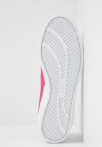 Semelle de chaussure blanche avec un motif de traction circulaire, des lignes de bande de roulement courbées et un logo rectangulaire central, sur fond blanc.