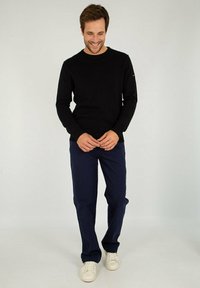 Maglione nero a maniche lunghe con scollo rotondo abbinato a pantaloni blu navy e sneakers bianche. L'outfit presenta un design slim fit e una texture liscia.