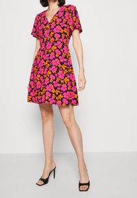 Kwiatowa sukienka na czarnym tle, z różowymi i pomarańczowymi kwiatami. Krótkie rękawy, głęboki dekolt w serek i rozkloszowana spódnica. Nosi ją w zestawieniu z czarnymi obcasami.