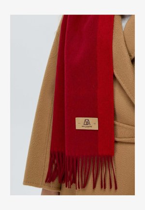 Roter Wollschal mit fransigen Enden, in rechteckiger Form. An ihm befestigt ist ein Lederschild mit der Prägung "BELLEMERE". Er wird über einem beigen Mantel getragen.