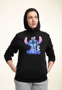 Felpa nera con cappuccio, con una grafica frontale di un personaggio dei cartoni animati blu, con dettagli rosa sulle orecchie e una texture morbida.