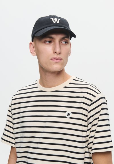 Czarna czapka z haftowanym logo, beżowy t-shirt w paski z krótkim rękawem, z okrągłym logo na piersi.