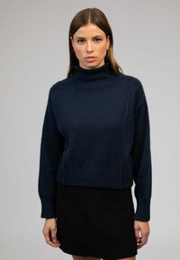 Pull en col roulé bleu marine avec un tissu texturé, des poignets et un ourlet côtelés, associé à une mini-jupe noire. Design simple, apparence chaleureuse.