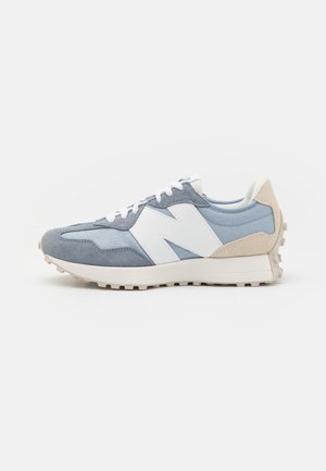 Lyseblå og grå sneaker med hvide snørebånd, en stor hvid "N"-logo på siden og en beige tekstureret hælkappe.