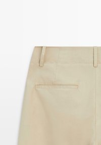 Beige skirt section showing back waistband with belt loops and a single horizontal welt pocket on a white background.