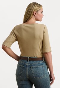 Top bej cu mânecă trei sferturi și decolteu rotund, asociat cu blugi din denim albastru, cu talie înaltă. Textură netedă și croială casual.