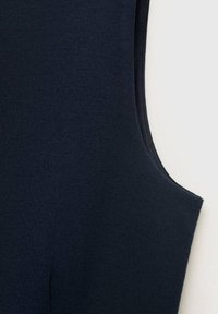 Námořnická modrá bezrukávová blůza s textura, těsně pleteným materiálem, kulatým výstřihem a zakřivenými průramky, která ukazuje hladkou siluetu.