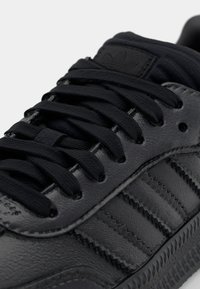 Närbild av svart lädersneaker med svarta snörningar och Adidass signatur tre ränder på sidan.