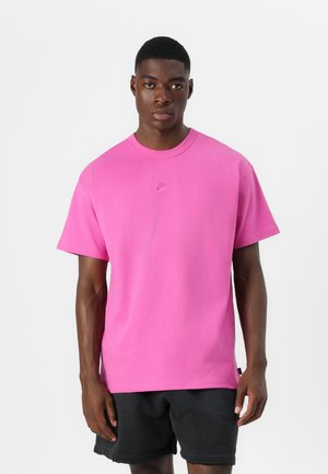 T-shirt en coton rose avec un col rond, des manches courtes et un petit logo Nike sur la poitrine ; porté avec un short noir.
