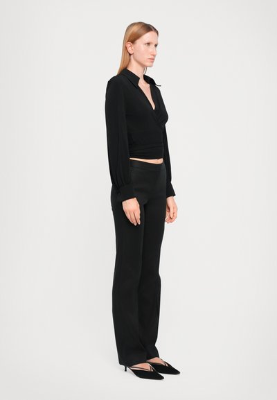 Blouse noire à manches longues, associée à un pantalon noir ajusté. Des escarpins noirs à bout pointu complètent la tenue. Tissu lisse et léger.