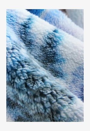 Zacht, pluizig deken in verschillende tinten blauw en wit, met een gestructureerd, donzig oppervlak en een verloopmotief.