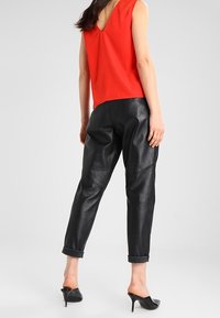 Rød ærmeløs top med V-hals, parret med sorte læderbukser med opsmøg. Høje sorte sko fuldender looket.