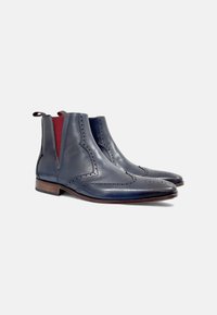 Botas de tobillo de cuero marino con detalles de brogue, paneles laterales elásticos y suelas de madera marrón, con un diseño elegante y de punta afilada.