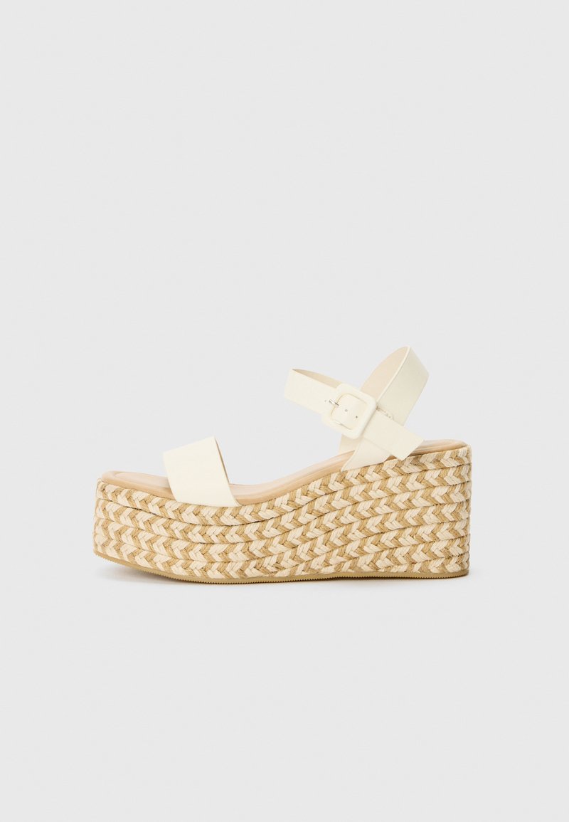 Sandales compensées blanches avec plateforme en jute tressé, dotées de deux larges brides et d'une sangle à la cheville avec boucle. Texture lisse, design décontracté.