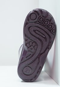 Semelle de chaussure en caoutchouc violet avec des motifs texturés, un détail d'empreinte de patte et un marqueur de taille "21" visible près du talon.