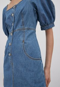 Denim-mekko, jossa on neliökaula-aukko, puffihihat ja nappikiinnitys. Mukana tyylikkäät ompeleet ja sivutaskut. Väri: keskimallinen sininen.