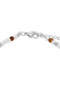Pulsera de cadena en tono plateado con perlas blancas y cuentas marrones. Cuenta con un cierre de langosta y una extensión de cadena para ajustar la longitud.