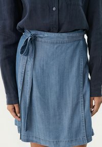Jupe en denim de couleur bleu clair avec une taille nouée. Présente une texture lisse, une coupe droite et un détail discret sur l'ourlet.