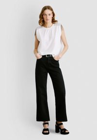 Valge pluus, millel on õlgade frillide detailid, kombineeritud kõrge vöökohaga mustade laiade pükstega ja mustade kontsakingadega. Lihtne ja modernne disain.